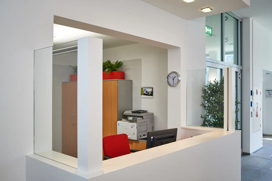 Moderne Rezeption mit Schreibtisch, Bürostuhl, Drucker und Pflanzen in hell eingerichteter Umgebung.