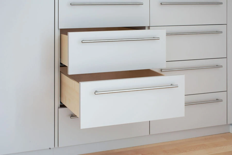 Detailaufnahme eines weißen Einbauschranks mit zwei offenen Schubladen und Edelstahlgriffen auf hellem Parkettboden.