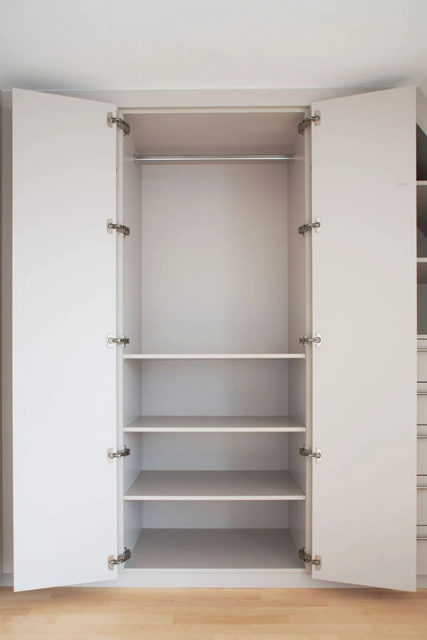 Geöffneter weißer Einbauschrank mit Kleiderstange und vier Einlegeböden zur flexiblen Aufbewahrung im Innenraum.