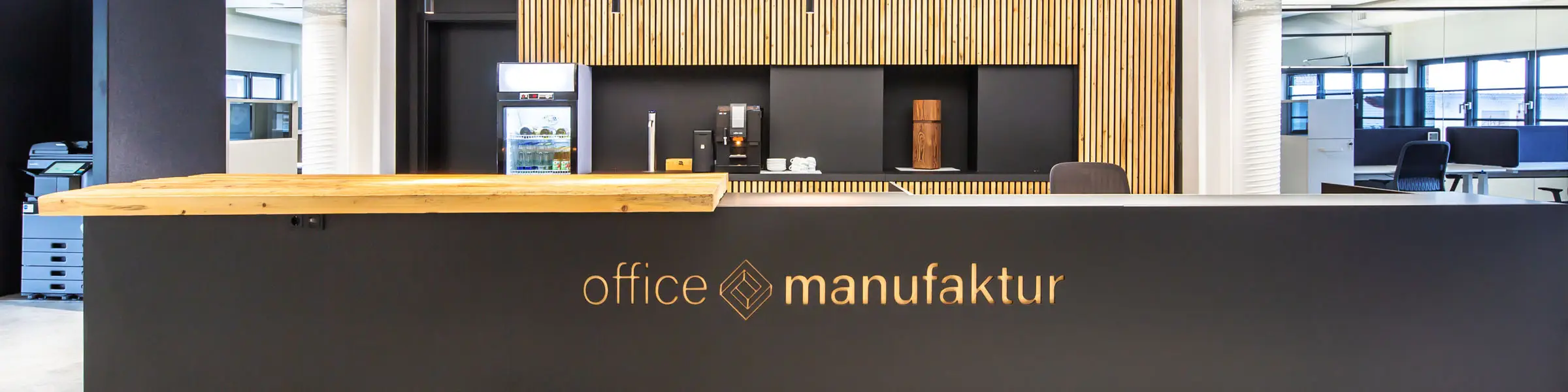 Moderne Empfangstheke der office manufaktur mit schwarzem Tresen, Holzverkleidung und offener Bürostruktur im Hintergrund.