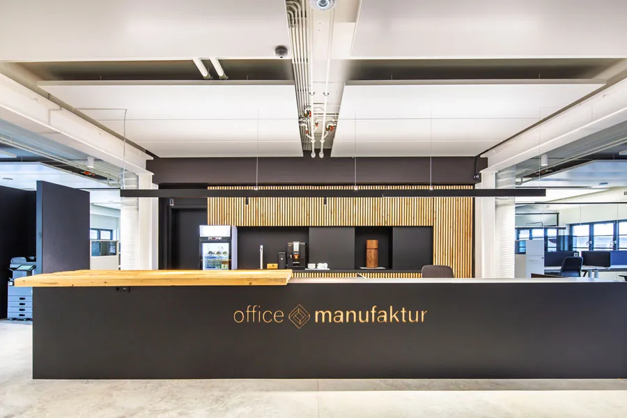 Moderne Empfangstheke der office manufaktur mit schwarzem Tresen, Holzverkleidung und offener Bürostruktur im Hintergrund.