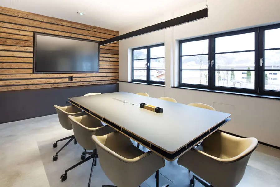Heller Besprechungsraum mit großem Konferenztisch, modernen Drehstühlen und Holzverkleidung mit integriertem Bildschirm.