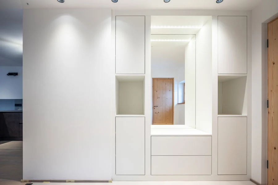 Moderner weißer Garderobenschrank mit integriertem Spiegel und indirekter LED-Beleuchtung im Eingangsbereich.