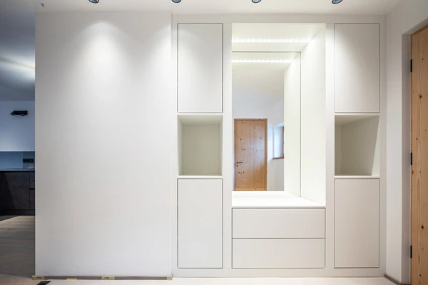Moderner weißer Garderobenschrank mit integriertem Spiegel und indirekter LED-Beleuchtung im Eingangsbereich.