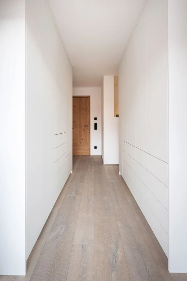 Moderner Flur mit deckenhohen, weißen Einbauschränken und hellem Holzfußboden.
