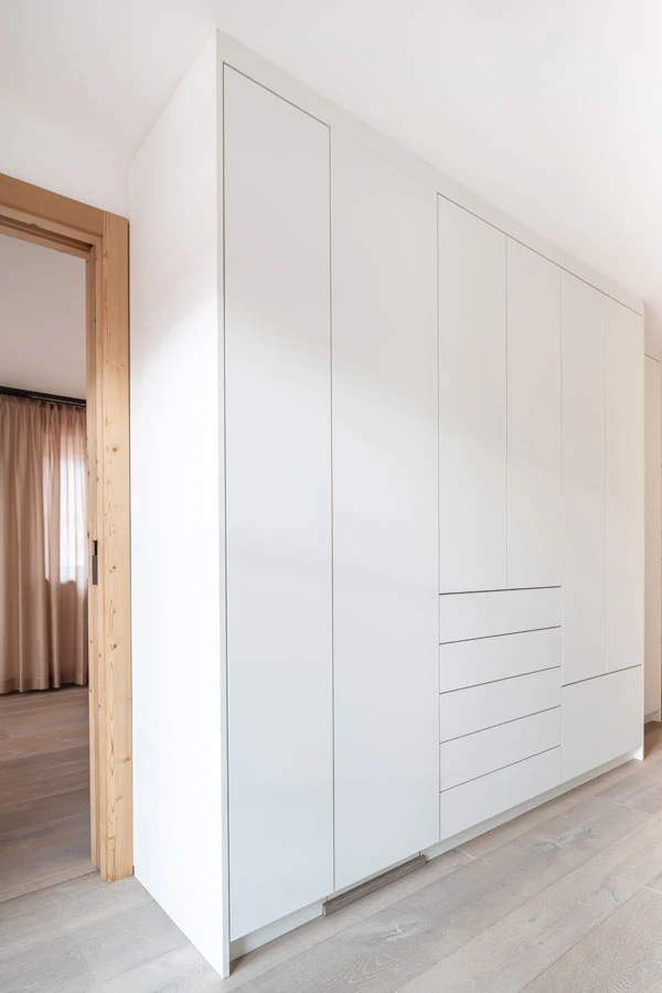 Schlichter, weißer Einbauschrank mit flächenbündigen Türen und Schubladen in einem modernen Schlafzimmer mit Holzdetails.