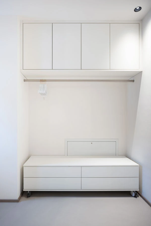 Minimalistische Garderobennische mit weißem Einbauschrank, Kleiderstange und rollbarer Kommode.