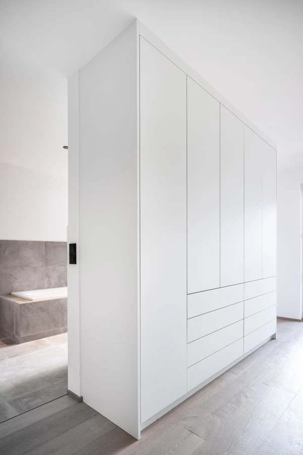 Moderner, weißer Einbauschrank mit grifflosen Fronten und Schubladen in einem hellen Flur mit direktem Zugang zum Badezimmer.