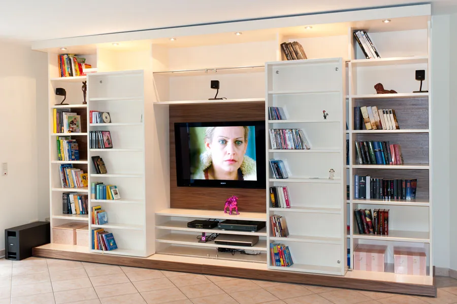 Moderne Medienwand mit integriertem Fernseher, offenen Regalen für Bücher und DVDs sowie verstecktem Stauraum in einem Wohnzimmer mit Fliesenboden.
