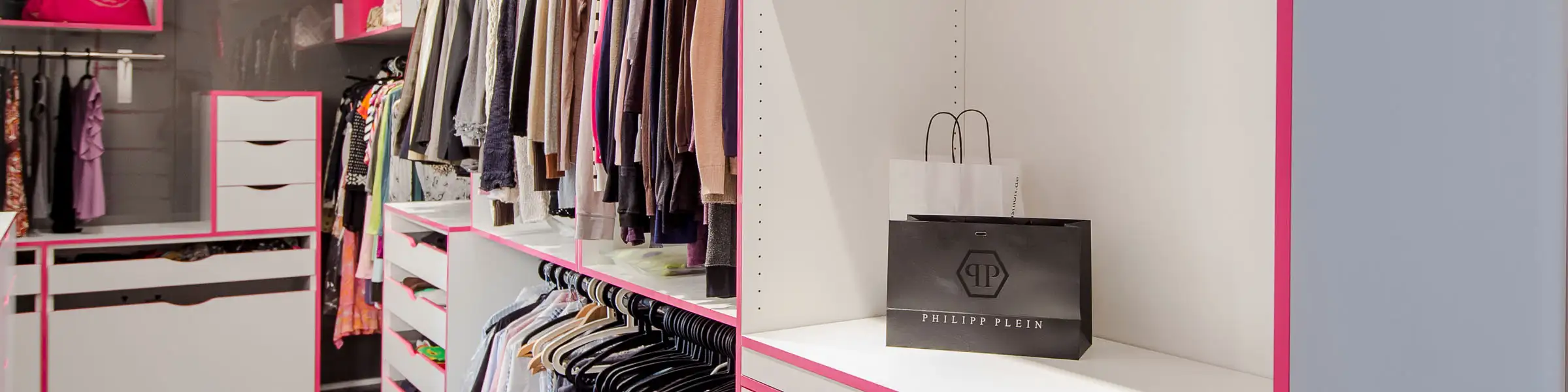 Begehbarer Kleiderschrank mit offenem Stauraum, Kleiderstangen und Schubladen in Weiß mit pinken Akzenten, modernem Design und dunklem Holzboden.