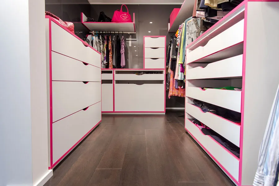 Modern gestalteter Ankleideraum mit offenen Schränken, Schubladen und Kleiderstangen in Weiß mit pinker Umrandung, kombiniert mit dunklem Parkettboden.