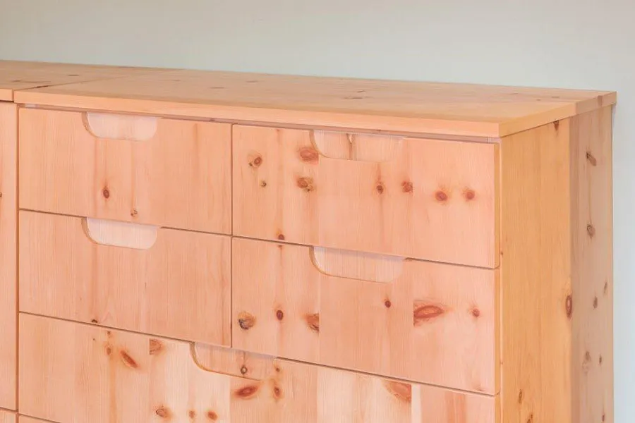 Detailaufnahme einer Kommode aus massivem Zirbenholz mit integrierten Griffmulden und natürlicher Holzmaserung im Schlafzimmer.