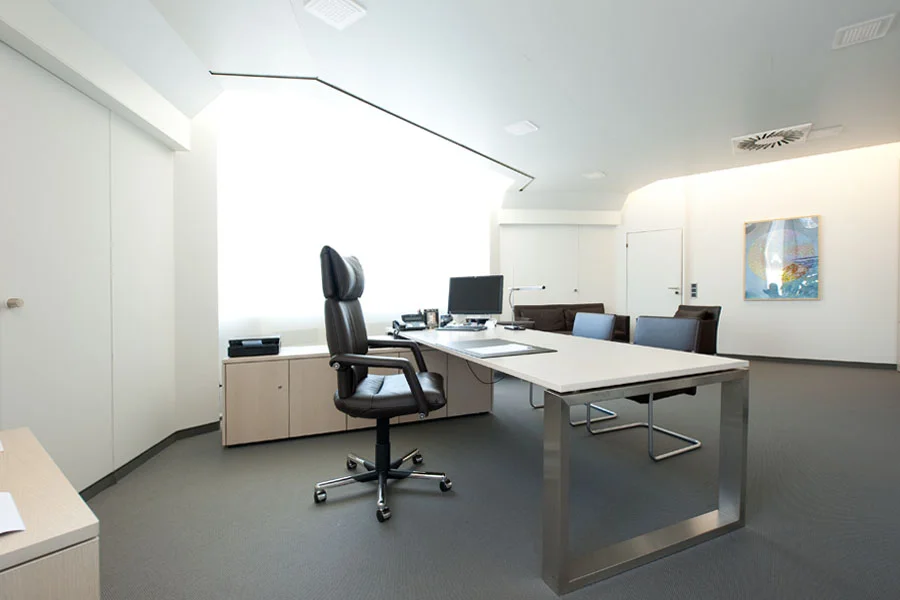 Helles und großzügiges Büro mit modernem Schreibtisch, Lederdrehstuhl und Besprechungsbereich – stilvolles Interieur unter Tageslichtkuppel mit Wandkunst.