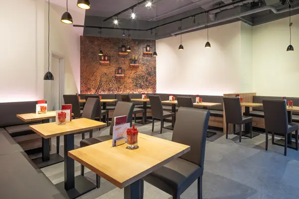 Modern eingerichtetes Restaurant mit hellen Holztischen, dunklen Polsterbänken und Designerleuchten – gemütliches Ambiente mit stilvoller Wandgestaltung.