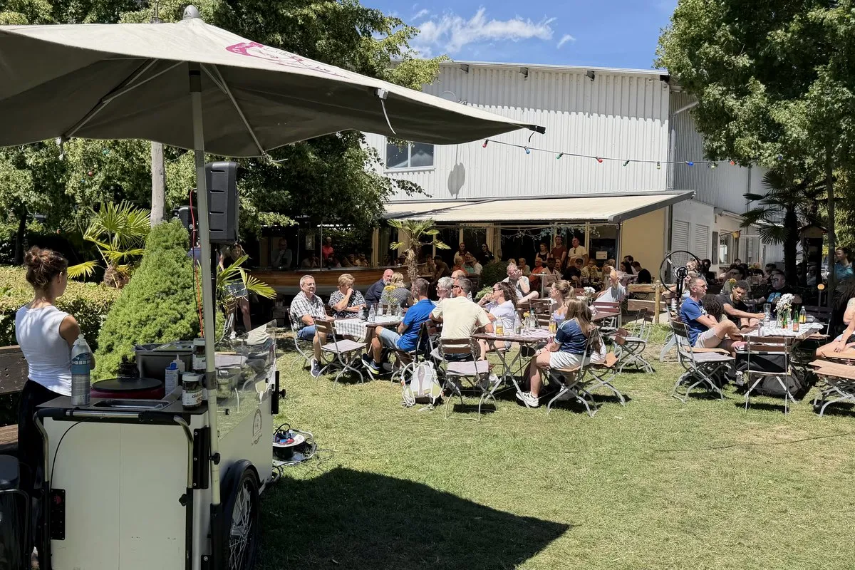 Sommerfest im Biergarten: volle Gästetische, Station mit Sonnenschirm