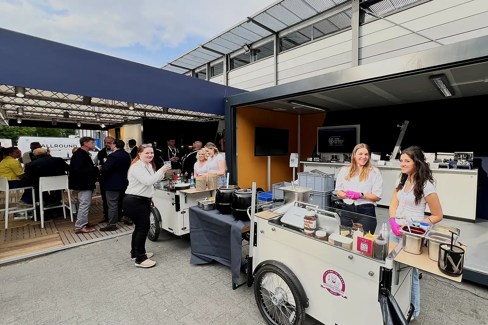 Firmenevent: Gäste in Businesskleidung an Stehtischen, daneben zwei CateringLovers-Stationen mit Crew im Einsatz.