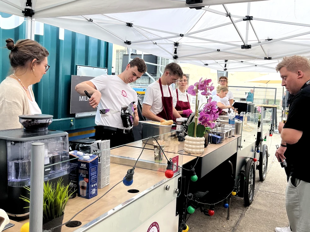 Zwei Kaffee-Stationen hintereinander unter weißen Faltzelten, Crew an der Espressomaschine, Gäste davor