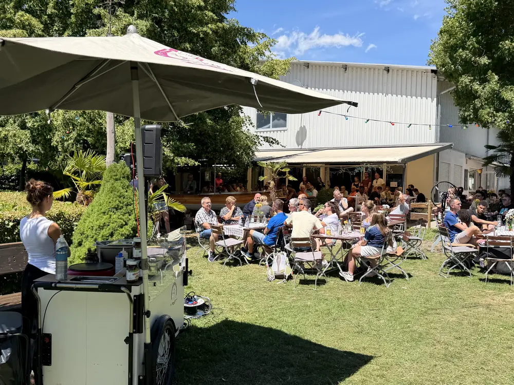 Sommerfest auf einer Wiese: HappyBike-Station unter Sonnenschirm, dahinter voll besetzte Gästetische