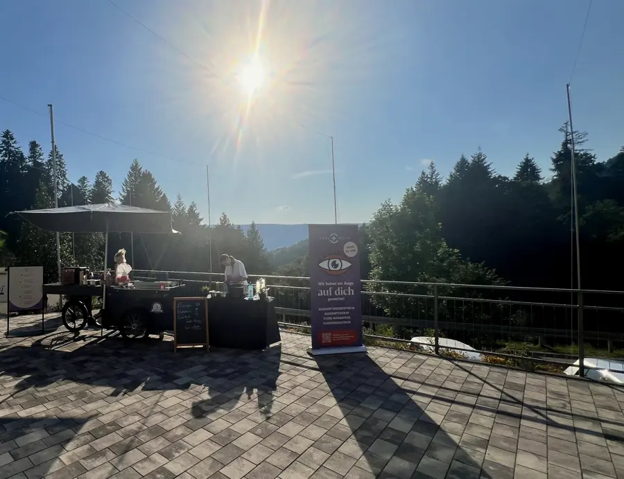 HappyBike-Station mit Schirm auf einer Terrasse über dem Tal, die Crew richtet die Ausgabe im Abendgegenlicht