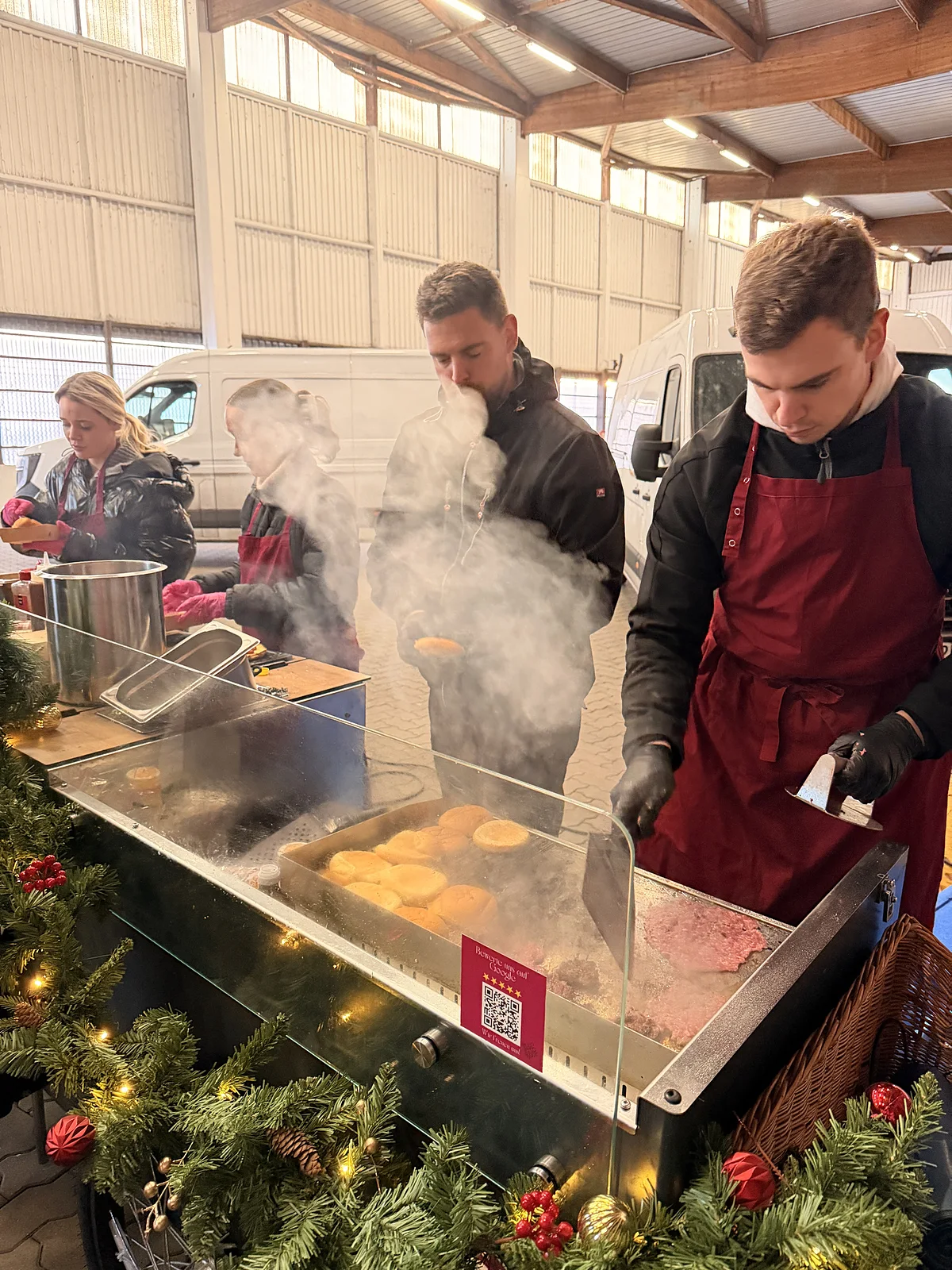 CateringLovers-Koch am dampfenden Grill mit Tannengirlande auf einer Weihnachtsfeier