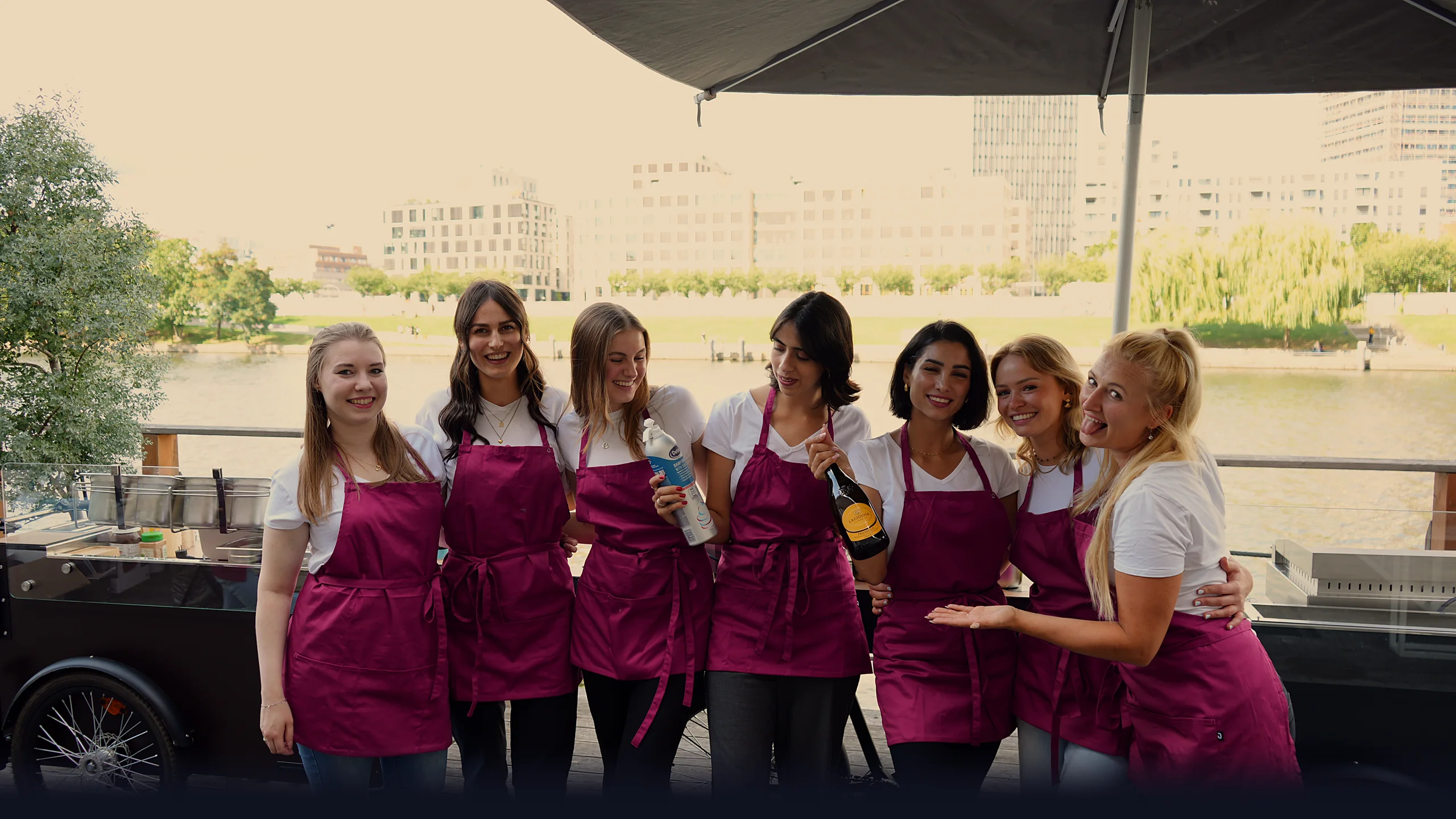 Sieben CateringLovers-Gastgeberinnen lachen im warmen Abendlicht am HappyBike an der Spree