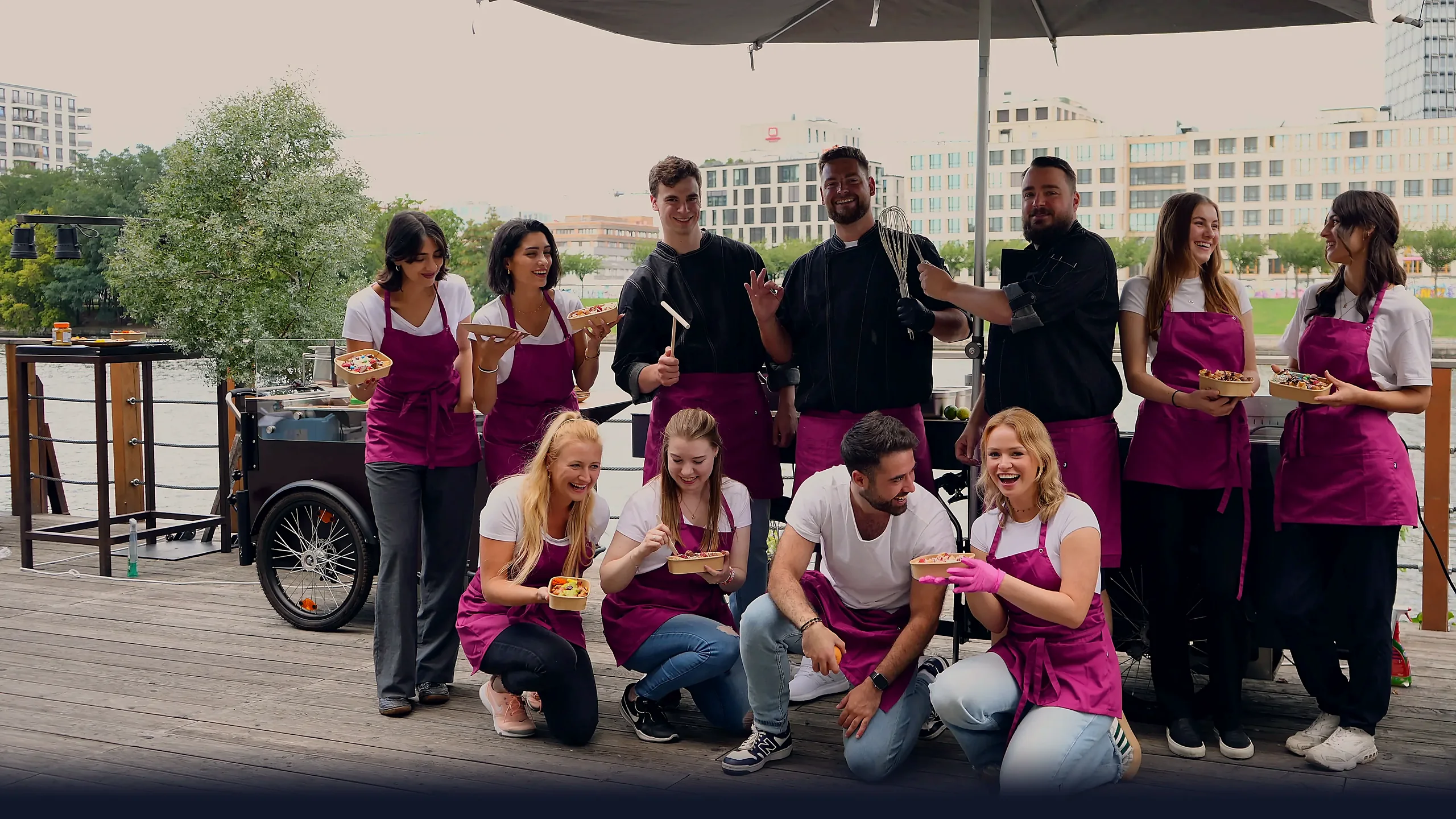 Das CateringLovers-Team an der Spree: Crew mit HappyBike vor der Berliner Skyline im warmen Licht