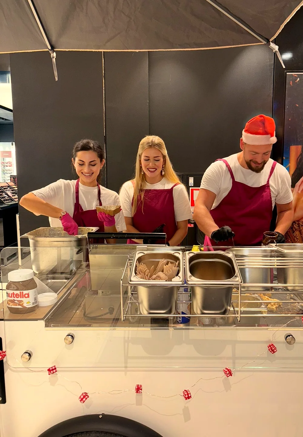 Drei CateringLovers-Crew-Mitglieder an der Station bei Galeria, einer mit Weihnachtsmütze, Lichterkette am HappyBike