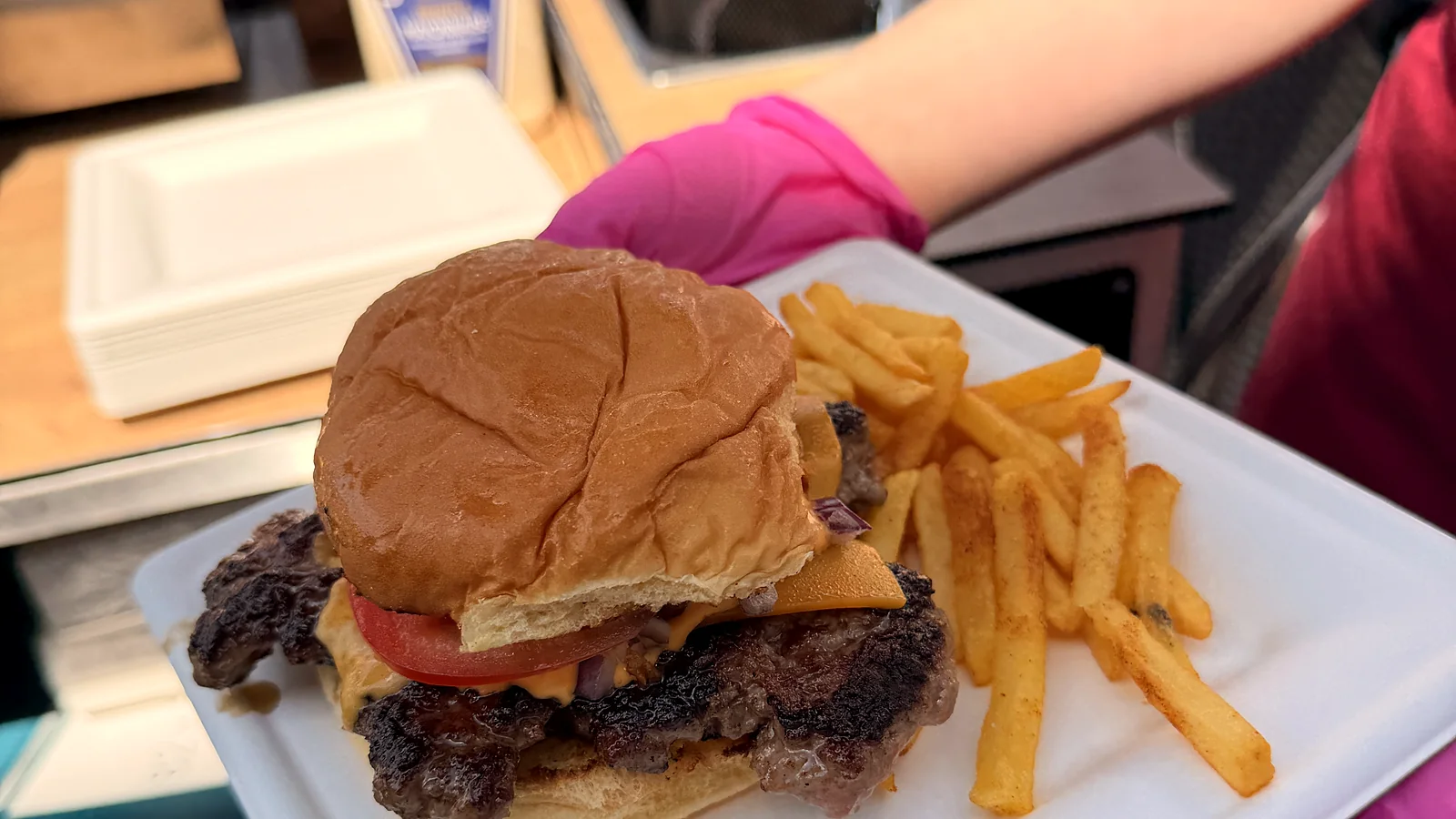 Burger mit Pommes wird auf dem Teller über die Station gereicht