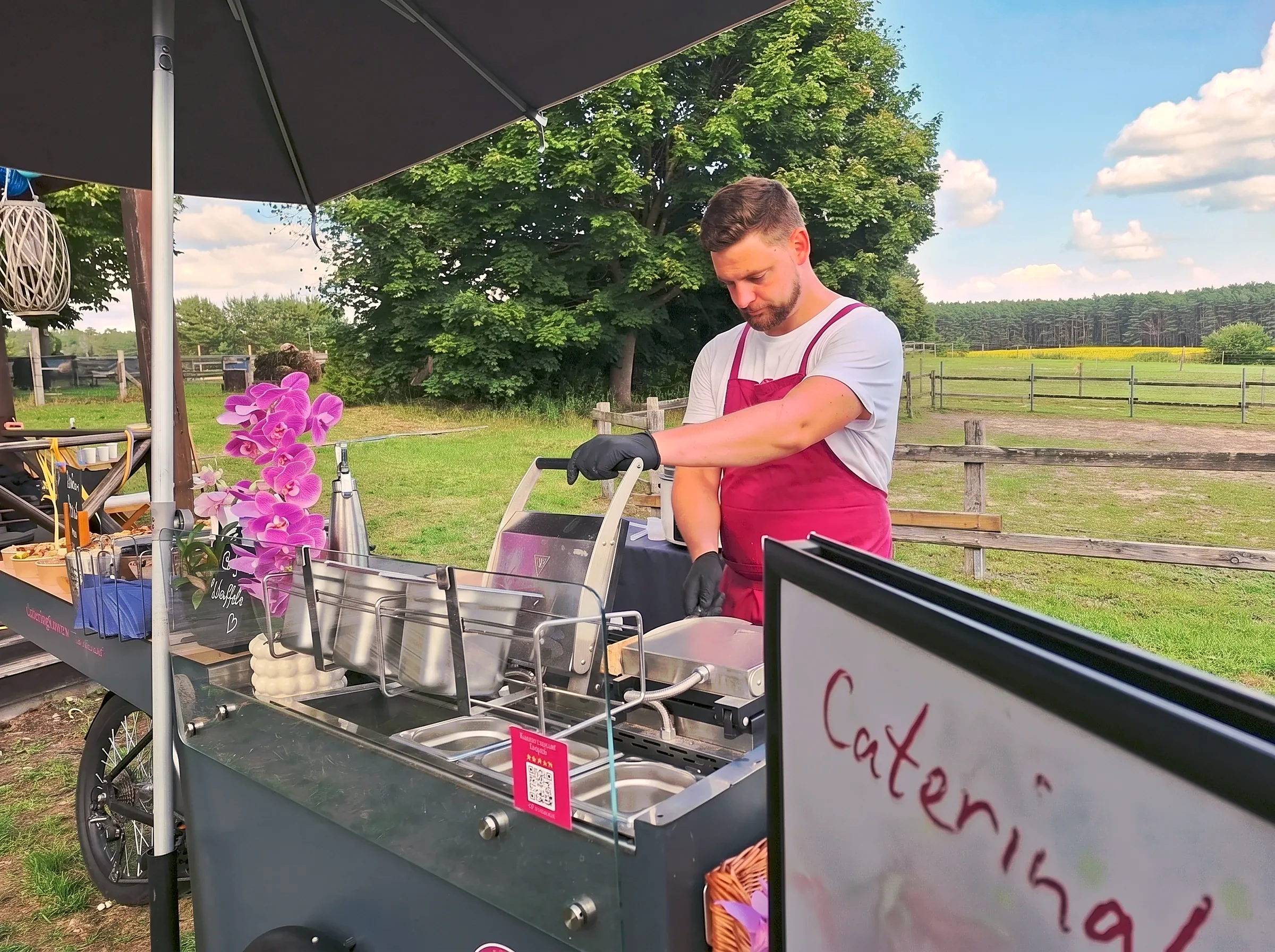 Mitarbeiter von CateringLovers kocht im Freien an einer HappyBike-Station, davor Edelstahlbehälter mit frisch zubereitetem Essen