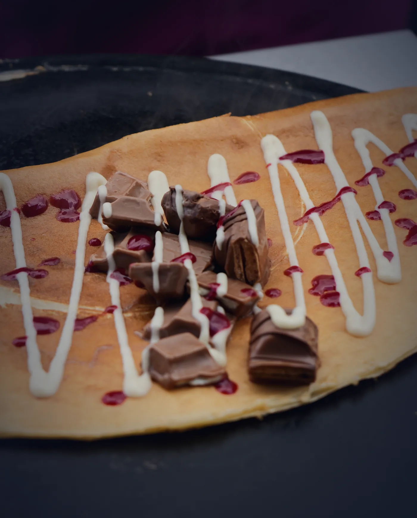 Crêpe mit Schokostücken, Himbeersoße und weißer Soße auf der heißen Platte