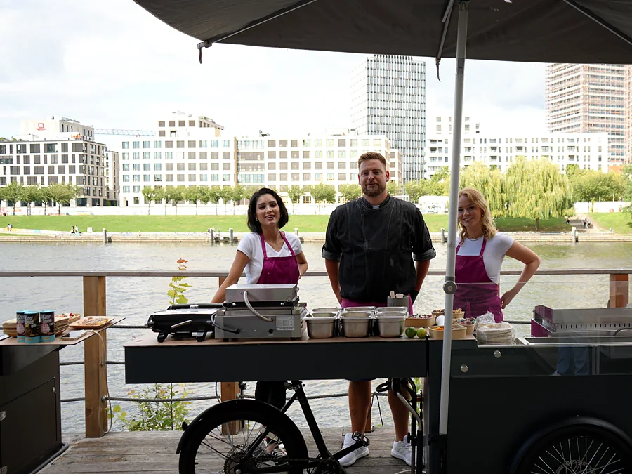 Drei Crew-Mitglieder von CateringLovers an ihrer Live-Cooking-Station am Wasser, unter dem Sonnenschirm