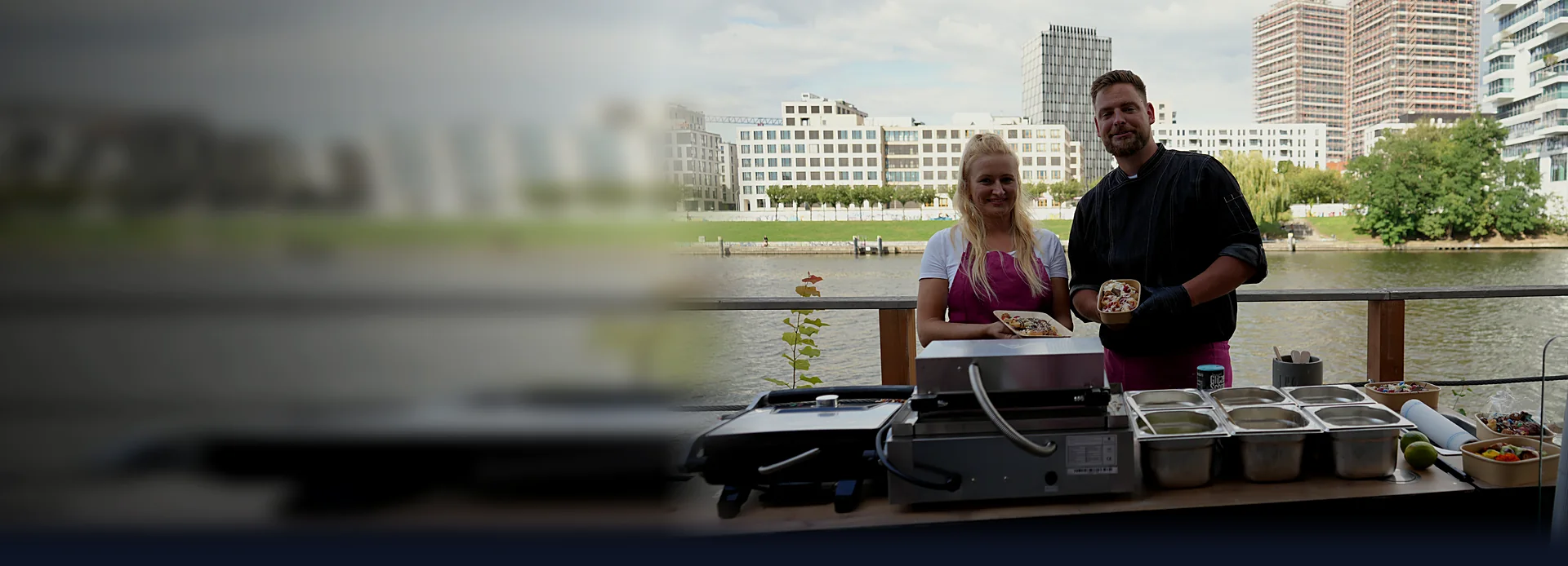 Zwei Crew-Mitglieder von CateringLovers an ihrer Live-Cooking-Station am Wasser, mit frisch angerichteten Bowls in der Hand