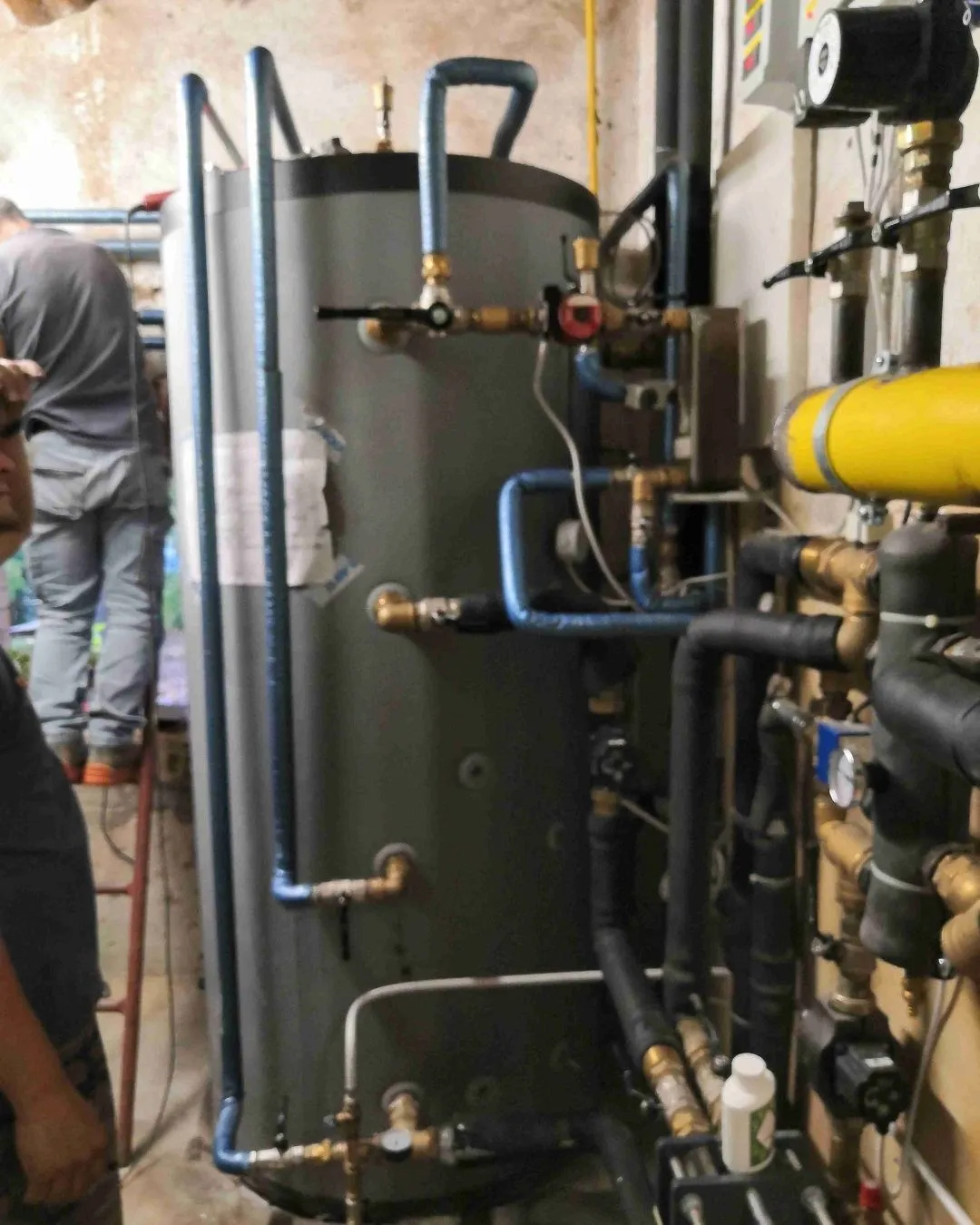 Tecnico installa o controlla un grande serbatoio con tubi e valvole in un locale tecnico.