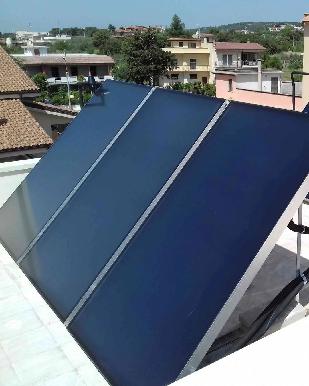 Pannello solare piatto installato su un tetto con edifici e alberi sullo sfondo.