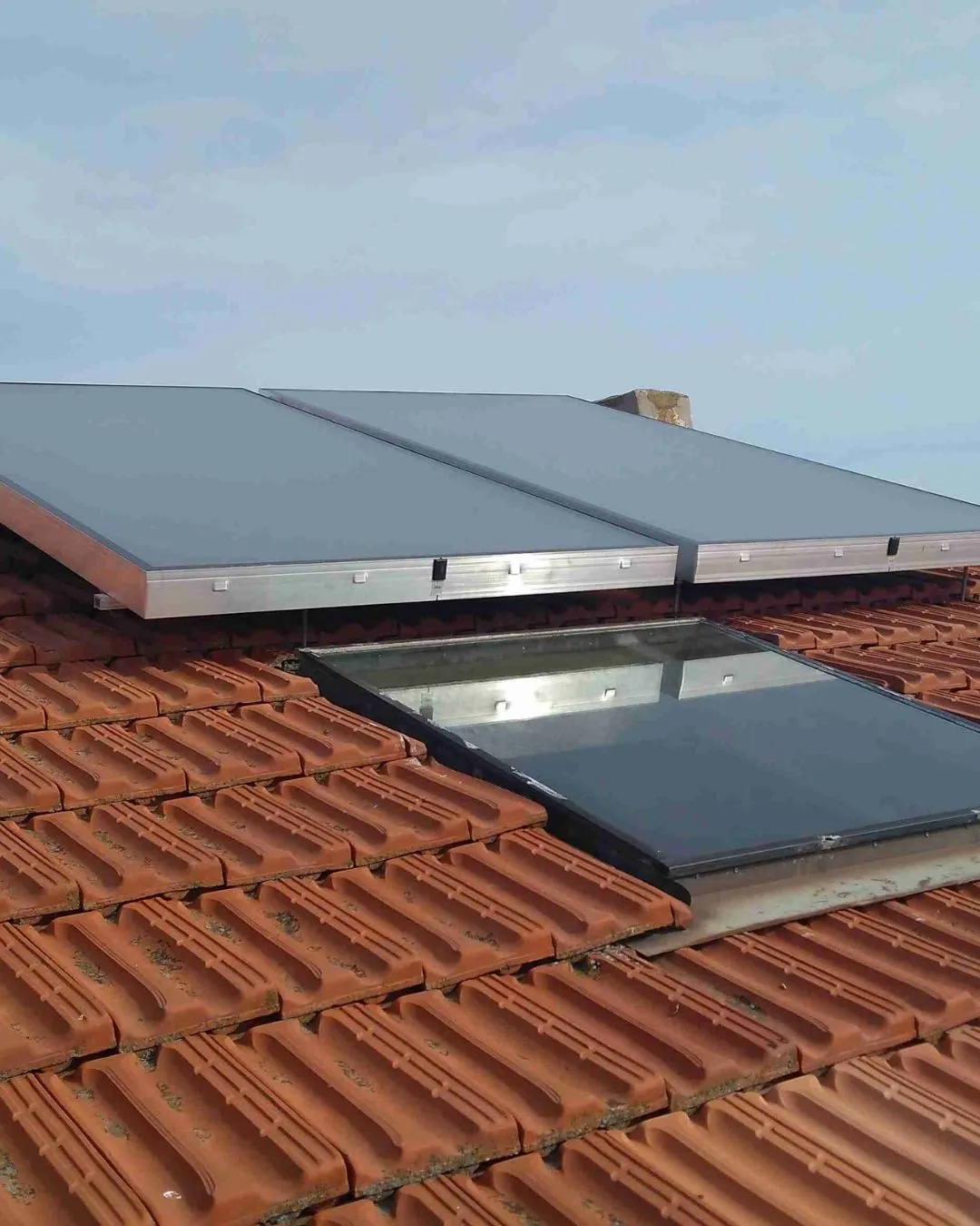 Pannelli solari installati sul tetto con tegole rosse e una finestra a tetto riflettente.