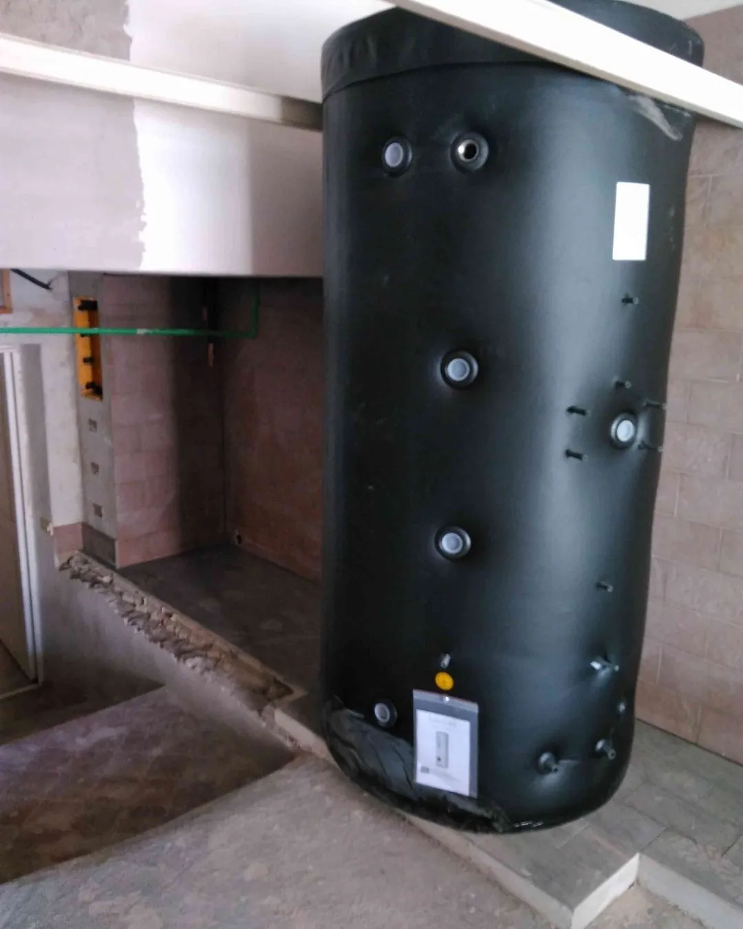 Serbatoio nero verticale per riscaldamento installato in un ambiente con pareti di piastrelle beige.