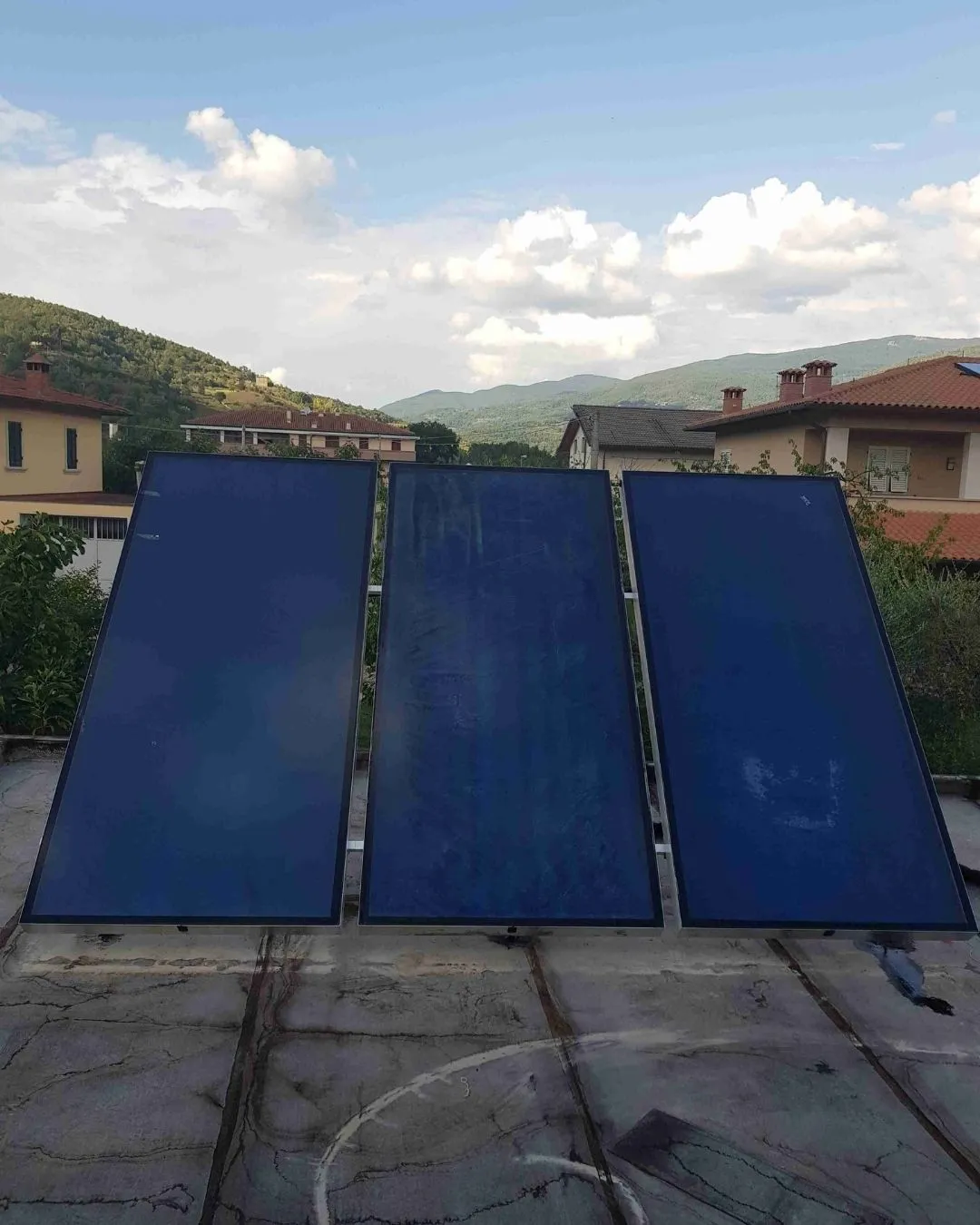 Tre pannelli solari installati su un tetto con case e colline sullo sfondo.