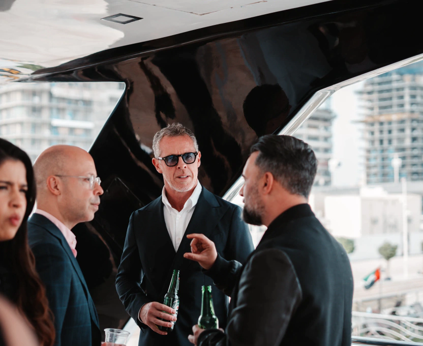 Four professionally dressed people conversing at an outdoor event, with two men holding bottles and a cityscape in the background.
