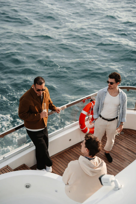 Three men casually standing and talking on a boat deck with ocean water in the background.