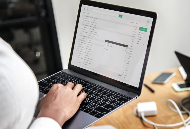 Person tippt auf Laptop und schreibt eine E-Mail, Posteingang mit mehreren Nachrichten ist sichtbar.