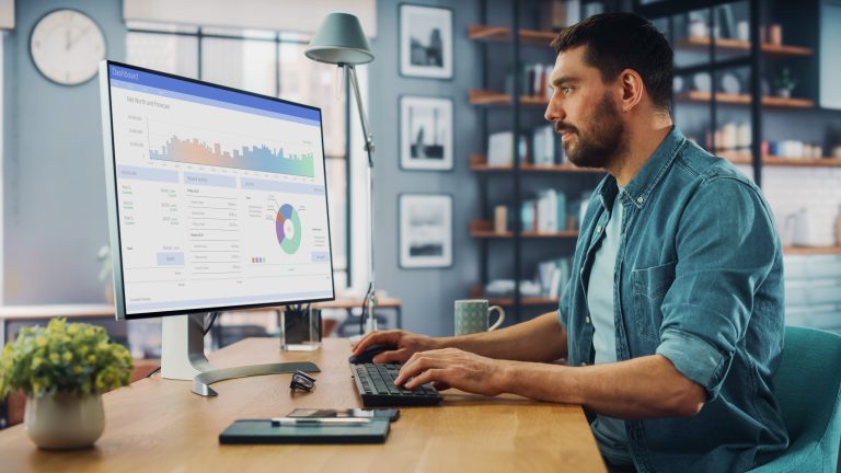 Jemand arbeitet am Schreibtisch und analysiert ein Dashboard mit Diagrammen auf einem großen Monitor.