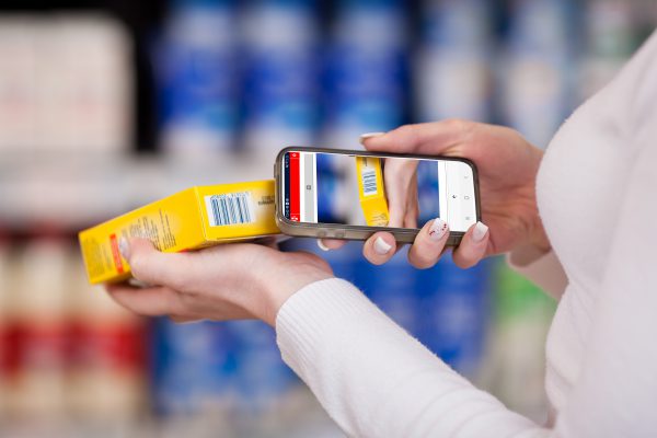 Person scannt mit Smartphone den Barcode auf einer gelben Verpackung.