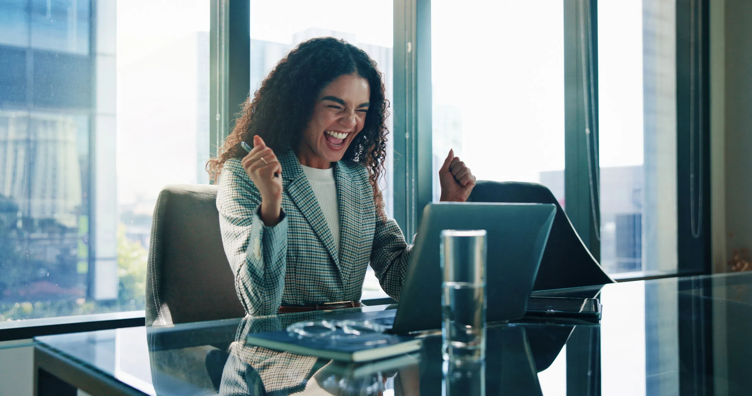 Frau im modernen Büro jubelt vor ihrem Laptop vor Freude.