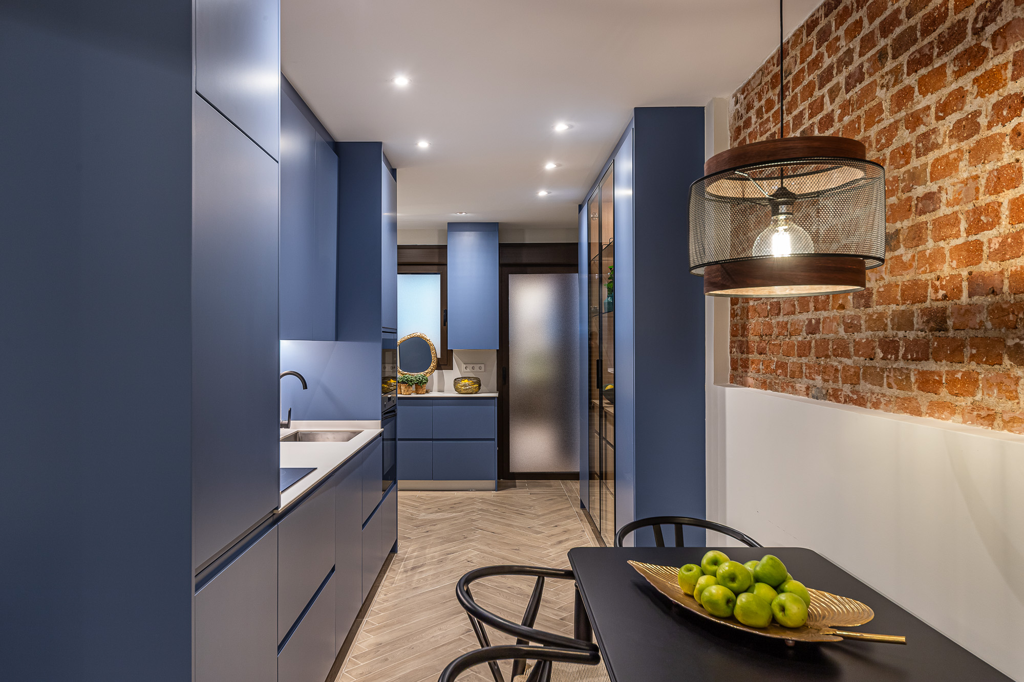 Cocina azul a medida con mesa de comedor negra junto al muro de ladrillo