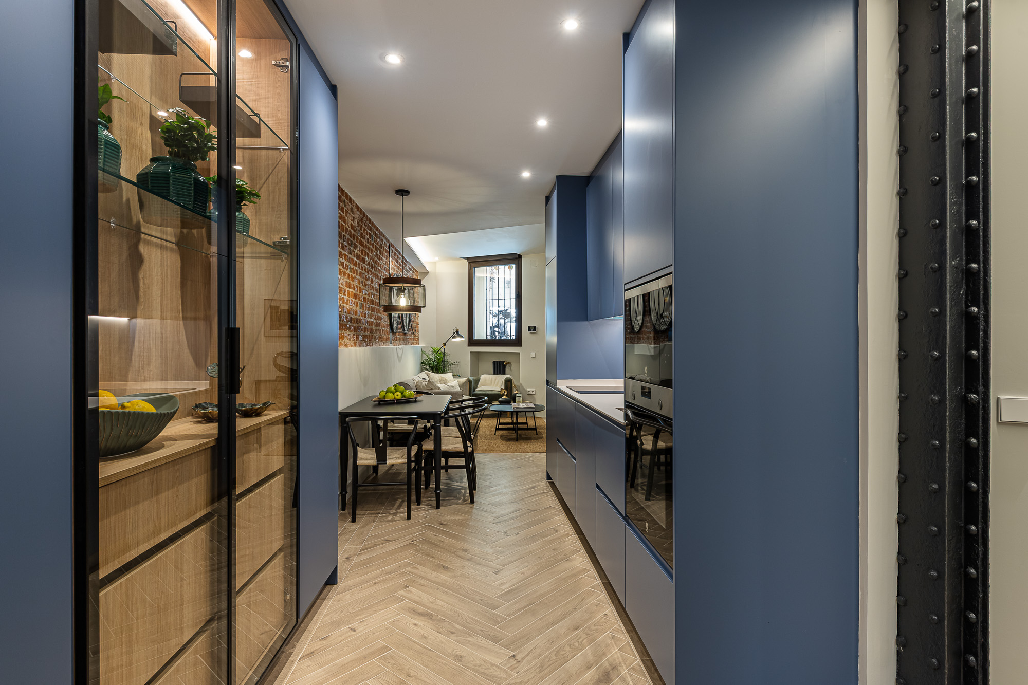 Cocina azul con vitrina de madera y vidrio, pilar de hierro remachado y vista al salón