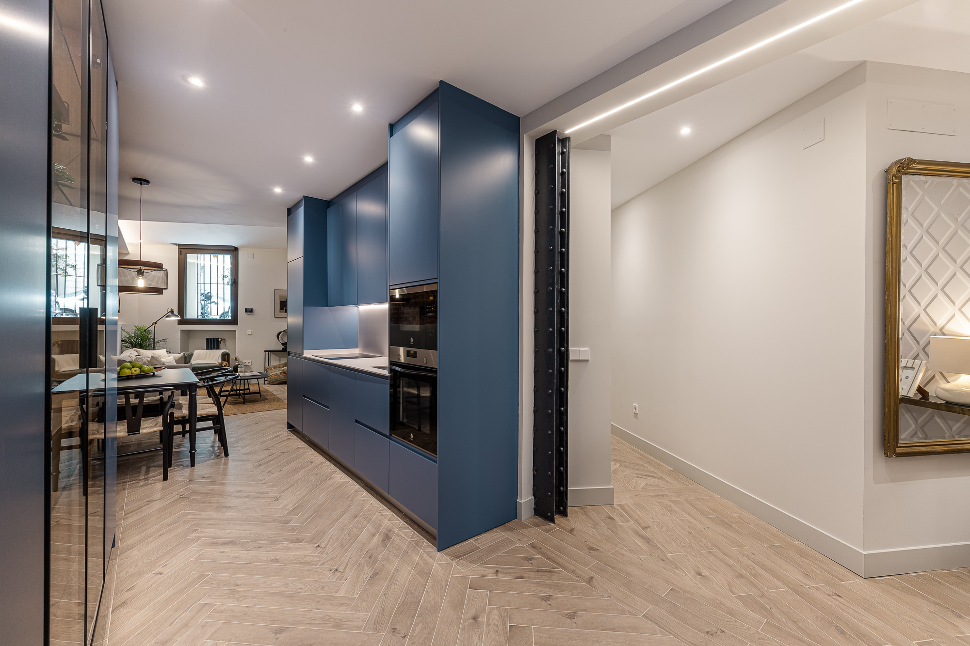 Cocina azul en primer término y pasillo con espejo dorado al fondo