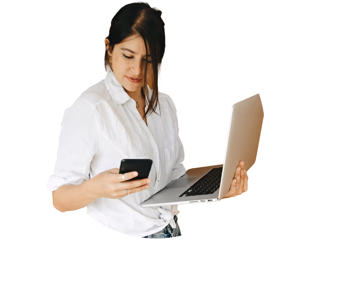Young woman in white shirt holding a laptop in one hand and looking at a smartphone in the other.