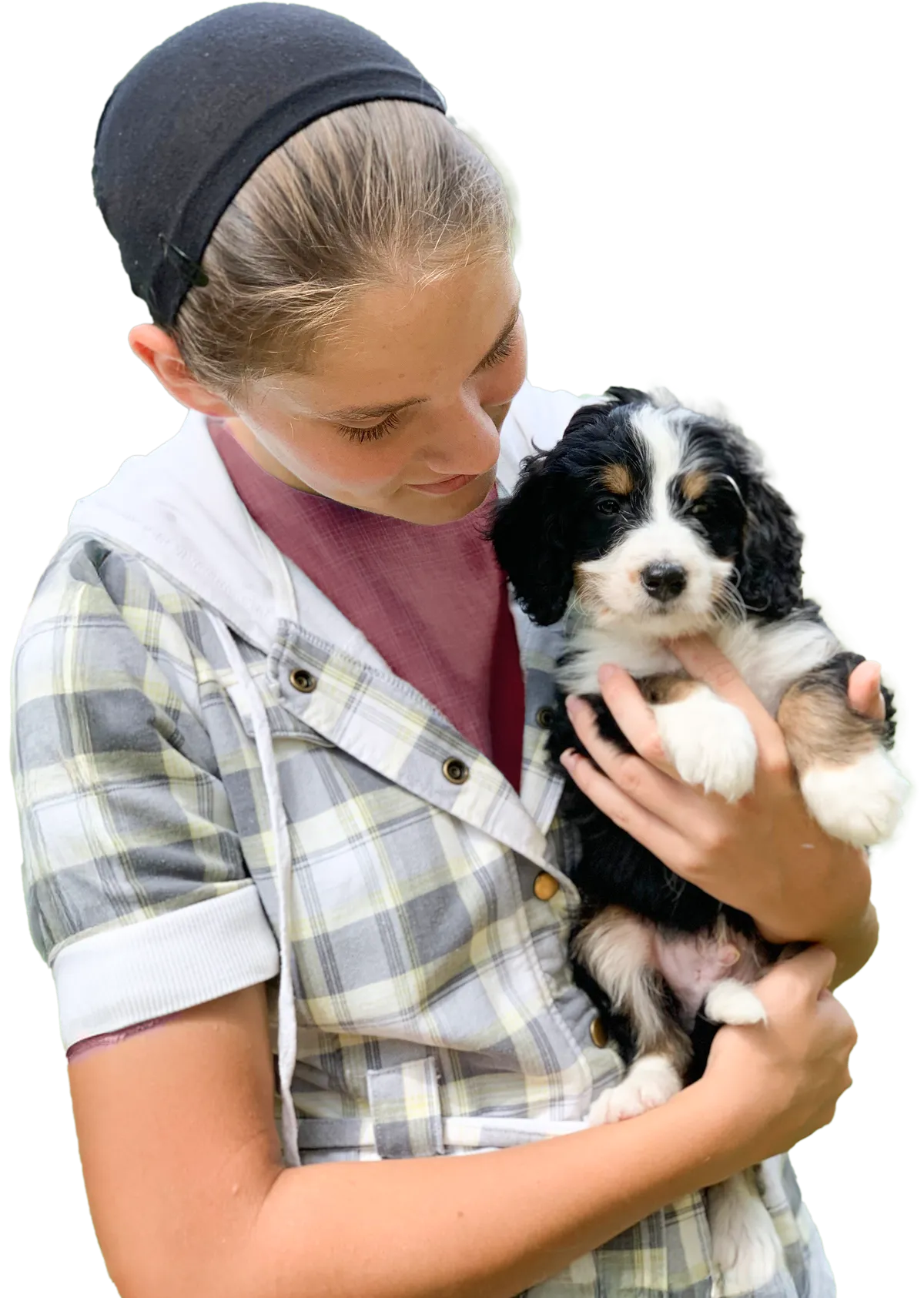 A young girl holds a small black, white, and brown puppy while looking down at it.
