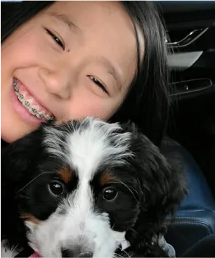 A girl with braces taking a selfie with a bernedoodle puppy.