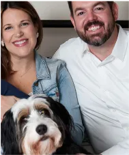 A happy couple posing for a picture with their puppy.